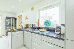 A modern kitchen with a large window, a blender, a kettle, and a bowl of fruit on the counter. - Family Fun Home: Hot Tub, Arcade, Game Room | 6BR (Cardiff)
