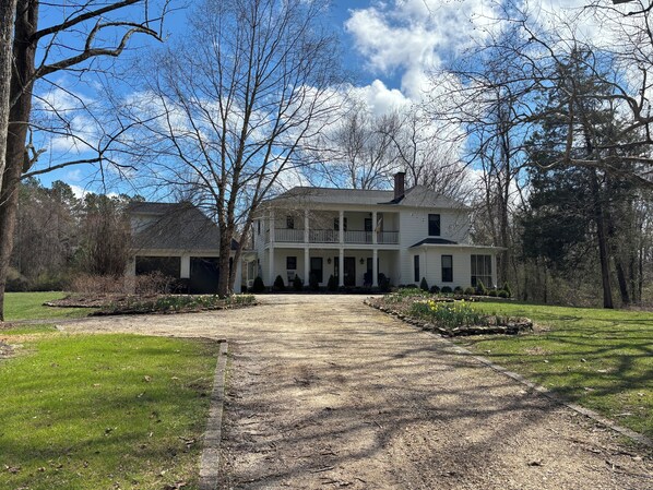 Una casa de dos pisos con un porche delantero, una entrada de vehículos y un jardín.