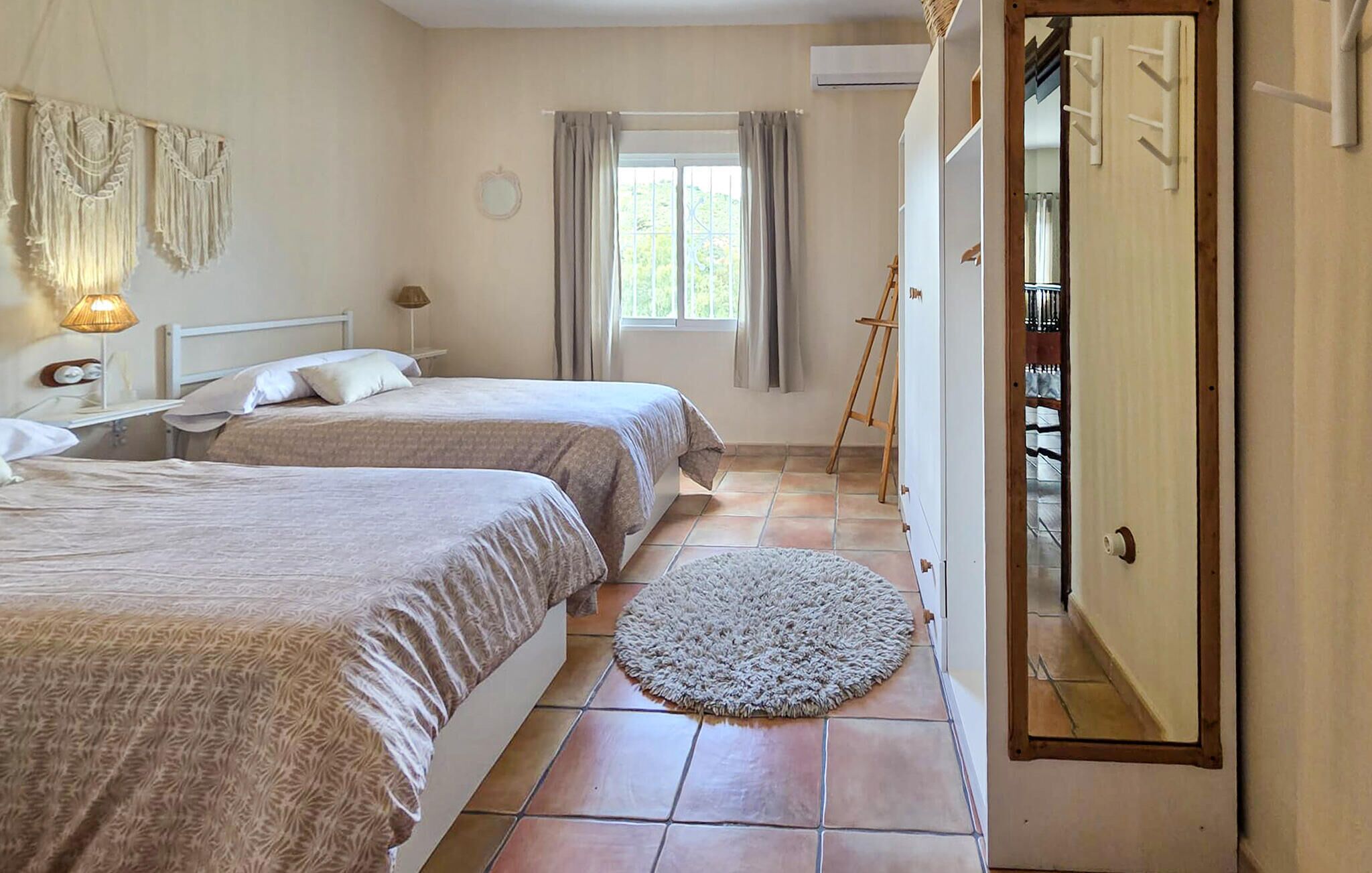 A bedroom with two beds, a window with curtains, a round rug, and a wooden ladder leaning against the wall.