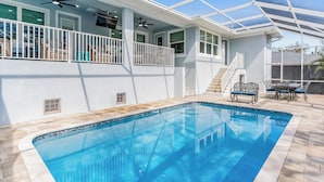 Une piscine entourée de parois en verre, un patio couvert avec des meubles d’extérieur et un escalier menant à un niveau supérieur.