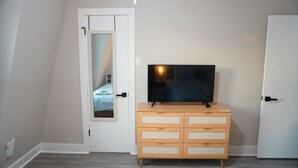 Makuuhuoneessa on puinen lipasto, jossa on televisio, peilillä varustettu ovi ja raidallinen vuodevaatteilla varustettu sänky.