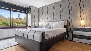 Quarto moderno com uma cama grande, mesas de cabeceira, cômoda e vista para o verde lá fora.