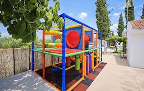 Estructura de juego con cerramiento de malla, un elemento circular rojo y una valla perimetral de bambú.