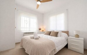 Un dormitorio con cama, mesitas de noche, ventilador de techo y ventana con vistas.
