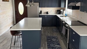 A modern kitchen with a central island, dark cabinets, and a wooden ceiling.