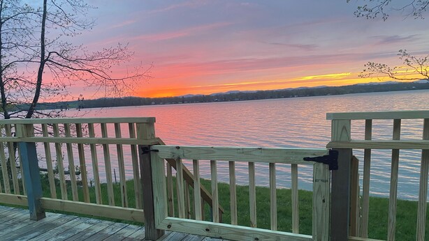 A wooden deck with a railing overlooking a body of water during sunset.