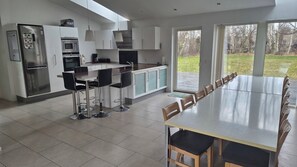 Een moderne keuken met roestvrijstalen apparatuur, een eethoek met een lange tafel en stoelen, en uitzicht op de omgeving.