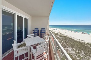 A balcony with a white table and chairs, overlooking a beach with umbrellas and people. - The Enclave 503 | Beachfront | Zero Entry Pool | Tennis Courts | My Beach Getaways (Orange Beach)