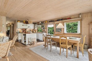 Een houten interieur met een eethoek, keuken en uitzicht op groen.