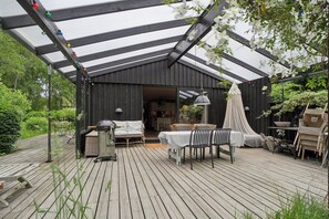Un espacio al aire libre cubierto con una terraza de madera, una mesa con sillas, una parrilla y un toldo.