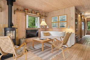 Een houten interieur met een open haard, een witte bank, rieten stoelen en een houten salontafel.