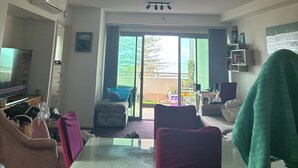 A living room with a glass door leading to an outdoor area, a ceiling-mounted air conditioner, and a flat-screen TV. - Coastal stay with great views (Redcliffe)