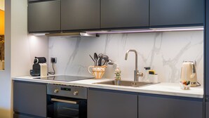 Une cuisine moderne avec des meubles de couleur sombre, un pare-feu en marbre, un four encastré et une machine à café.