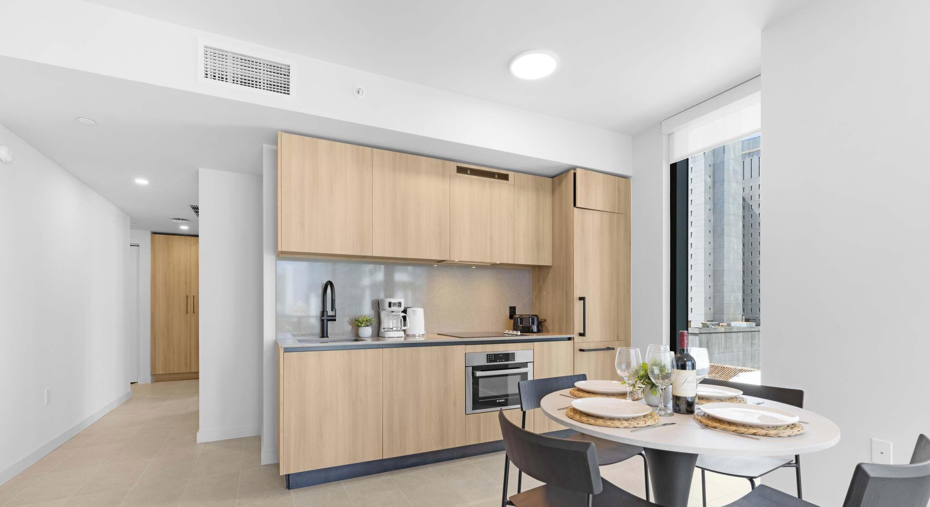 Une cuisine moderne avec des meubles en bois, un four encastré et un coin repas comprenant une table ronde et des chaises.