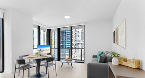 A modern living room with a dining area, large windows, and a view of high-rise buildings. - Balcony Mornings  Resort Living  1BR (Miami)