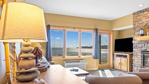 Ein Wohnzimmer mit Kamin aus Stein, einem Fernseher und Blick auf den Strand.