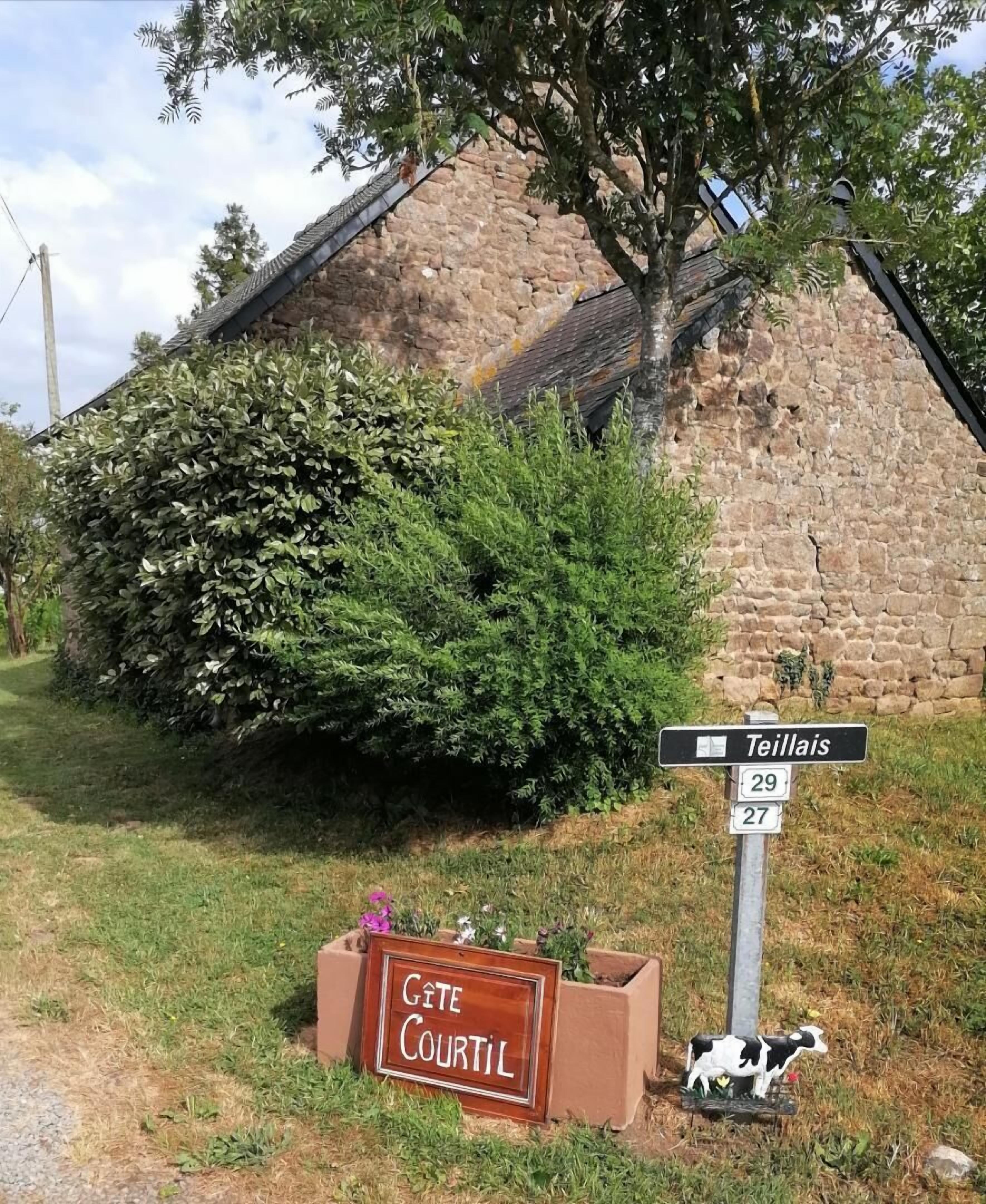 Een stenen gebouw met een bord dat de richting naar Teillais en Gîte Courtil aangeeft.