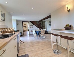 A modern kitchen with a dining area, wooden flooring, and a staircase leading to an upper level. - Le Courtil - SAINT SAUVEUR DES LANDES (SAINT SAUVEUR DES LANDES)