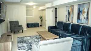 A living room with a sectional sofa, a small table, a chair, and a TV mounted on the wall. - Private Basement Suite Near Metro, See the Best of Silver Spring (Silver Spring)