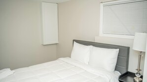 A neatly made bed with white bedding, a grey headboard, and a bedside table with a lamp. - Private Basement Suite Near Metro, See the Best of Silver Spring (Silver Spring)