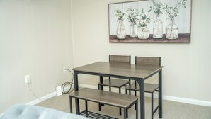 A dining area with a wooden table and benches, a power outlet, and a wall-mounted painting of vases with flowers. - Private Basement Suite Near Metro, See the Best of Silver Spring (Silver Spring)