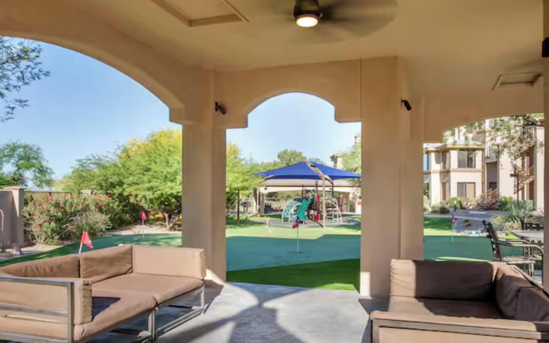 Un espacio de estar al aire libre cubierto con vista a un parque infantil y un edificio al fondo.