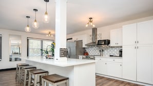 A modern kitchen with white cabinetry, a central island with stools, pendant lighting, and a visible kitchen island sign. - 5BR/3BA Stylish Modern Home in Decatur (Decatur)