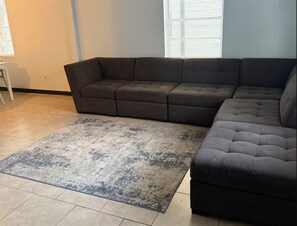 Ein Ecksofa, ein Teppich und ein Fenster mit Jalousien.