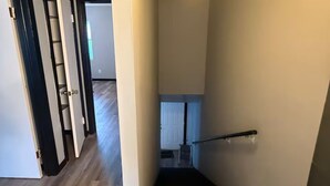 Un pasillo con suelo de madera, una barandilla negra y una puerta blanca a la izquierda.