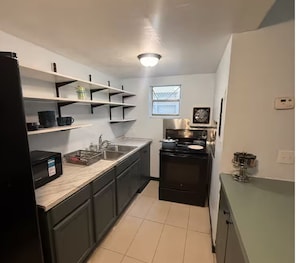 A compact kitchen with a sink, stove, and shelves.