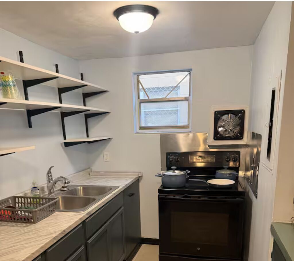 A compact kitchen with a stainless steel sink, a stove, and a window above the sink.