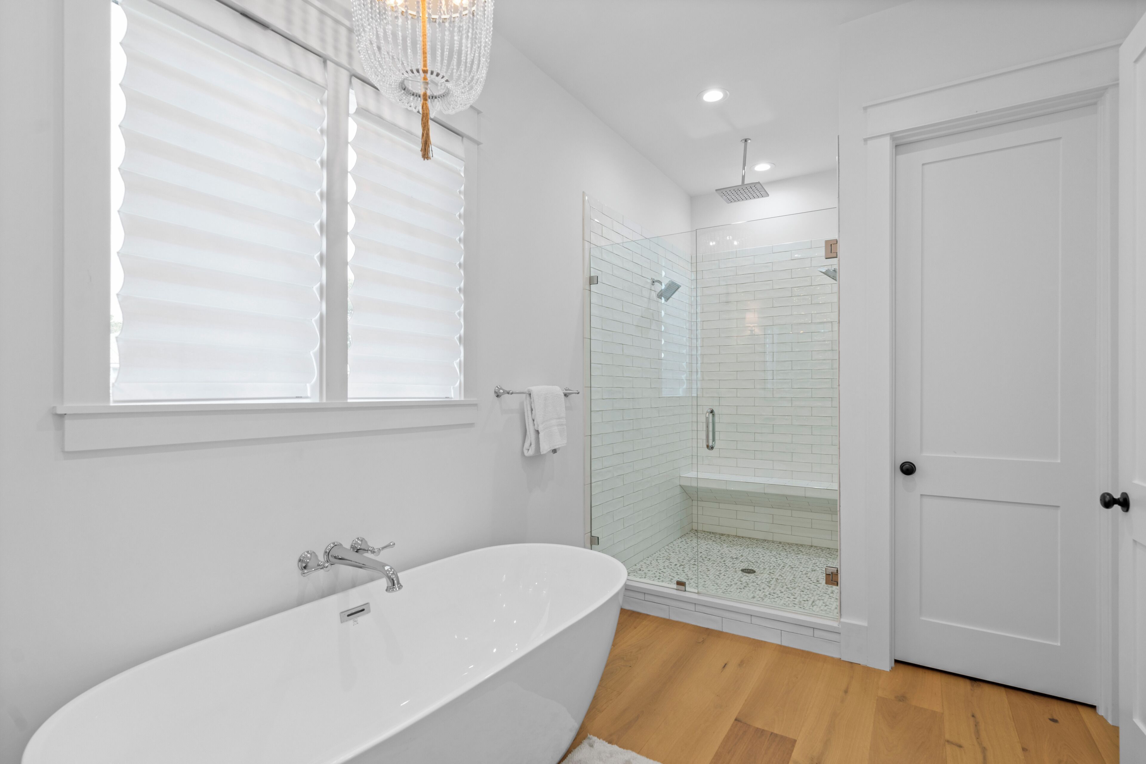 Ein modernes Badezimmer mit einer freistehenden Badewanne, einer in Glas abgeschirmten Dusche und einer weißen Tür.
