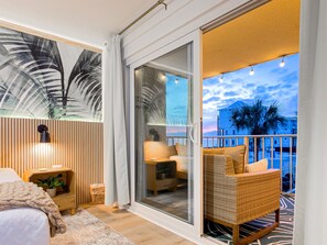 A balcony with wicker furniture, a sliding glass door, and a view of palm trees and buildings. - NEW! 3 Pools | Tiki Bar | 2nd Floor | Sleeps 10 | Renovated! (Panama City Beach)