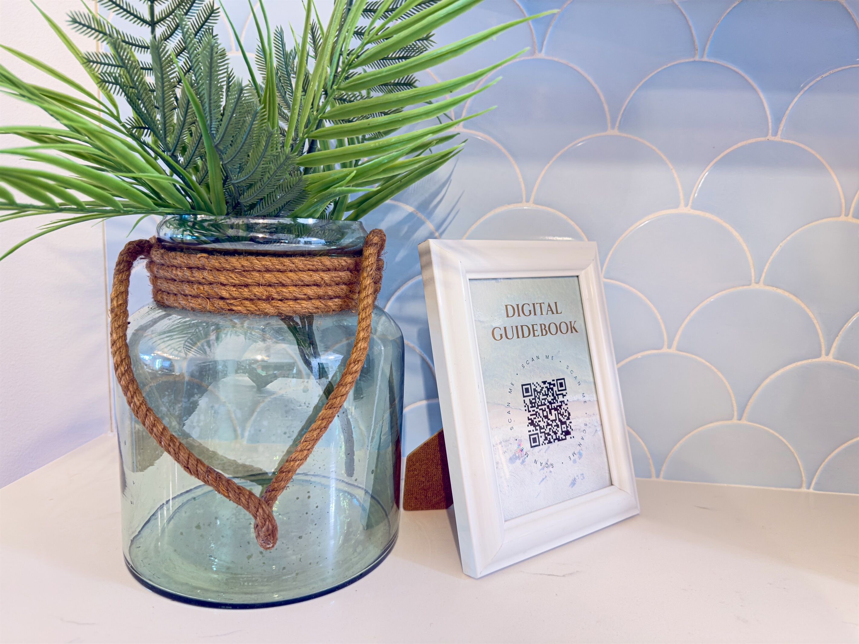 Un bocal en verre avec une anse en corde, un code QR encadré et une plante.