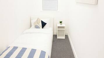 A hotel room with a bed, a small bedside table with a plant, a window with blinds, and a world map on the wall.
