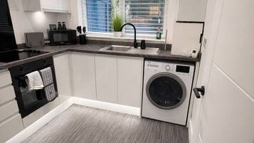 A compact kitchen with a built-in washing machine, a sink, and a window with blinds.