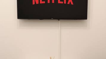 A flat-screen TV mounted on a wall with the Netflix logo, a marble coffee table with a tray and remote, and a carpeted floor.