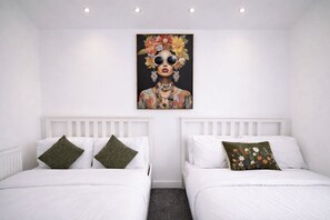 Habitación de hotel con dos camas, ropa de cama blanca y una obra de arte floral sobre las camas.