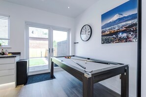 Ein Billardtisch in einem Raum mit Blick auf die Stadtlandschaft, eine Uhr an der Wand und eine Tür zu einem Außenbereich.