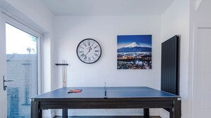 Et bordtennisbord i et rum med et ur og et bybillede på væggen.