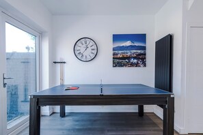 A ping pong table in a room with a clock and a cityscape painting on the wall. - Modern Home for 9 with Garden (Greater Manchester)