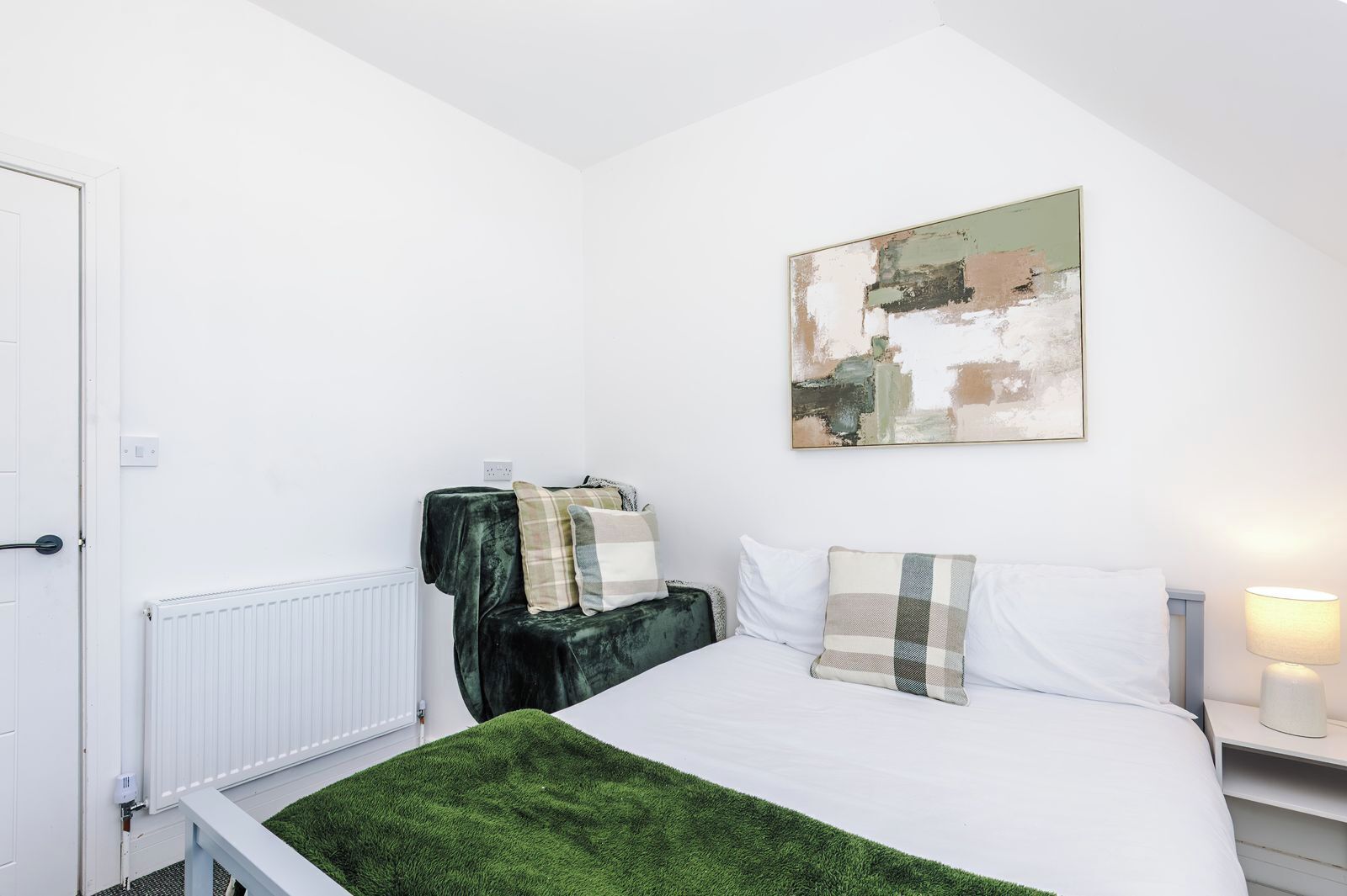 A bedroom with a bed, a radiator, a green rug, and a painting on the wall.