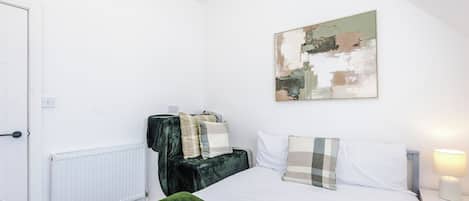 A bedroom with a bed, a radiator, a green rug, and a painting on the wall.