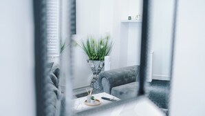 En moderne stue med en grå sofa, et sofabord med en plante, og en hvid væg med en radiator.