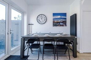 A dining area with a table set for four, a wall clock, and a framed picture of a mountain. - Modern Home for 9 with Garden (Greater Manchester)