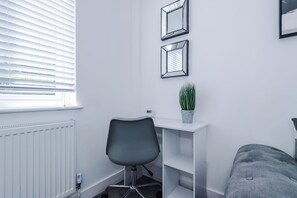 A room with a white desk, a grey office chair, a potted plant, and a grey sofa. - Modern Home for 9 with Garden (Greater Manchester)