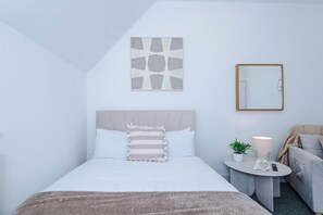 A bedroom with a bed, a bedside table with a lamp, a small potted plant, and a mirror on the wall. - Modern Home for 9 with Garden (Greater Manchester)