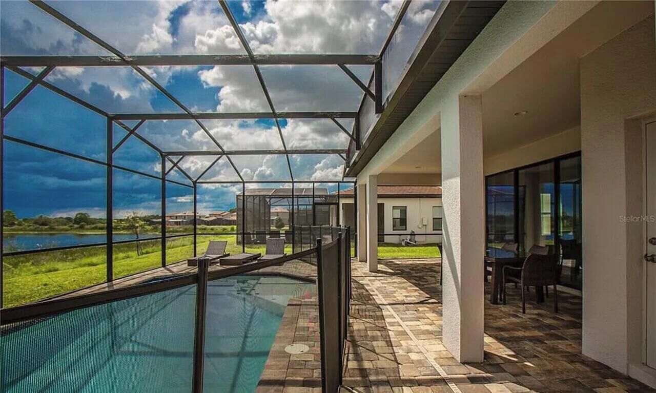 Une piscine extérieure couverte avec vue sur un lac, un espace patio avec des chaises et un bâtiment doté de grandes fenêtres.
