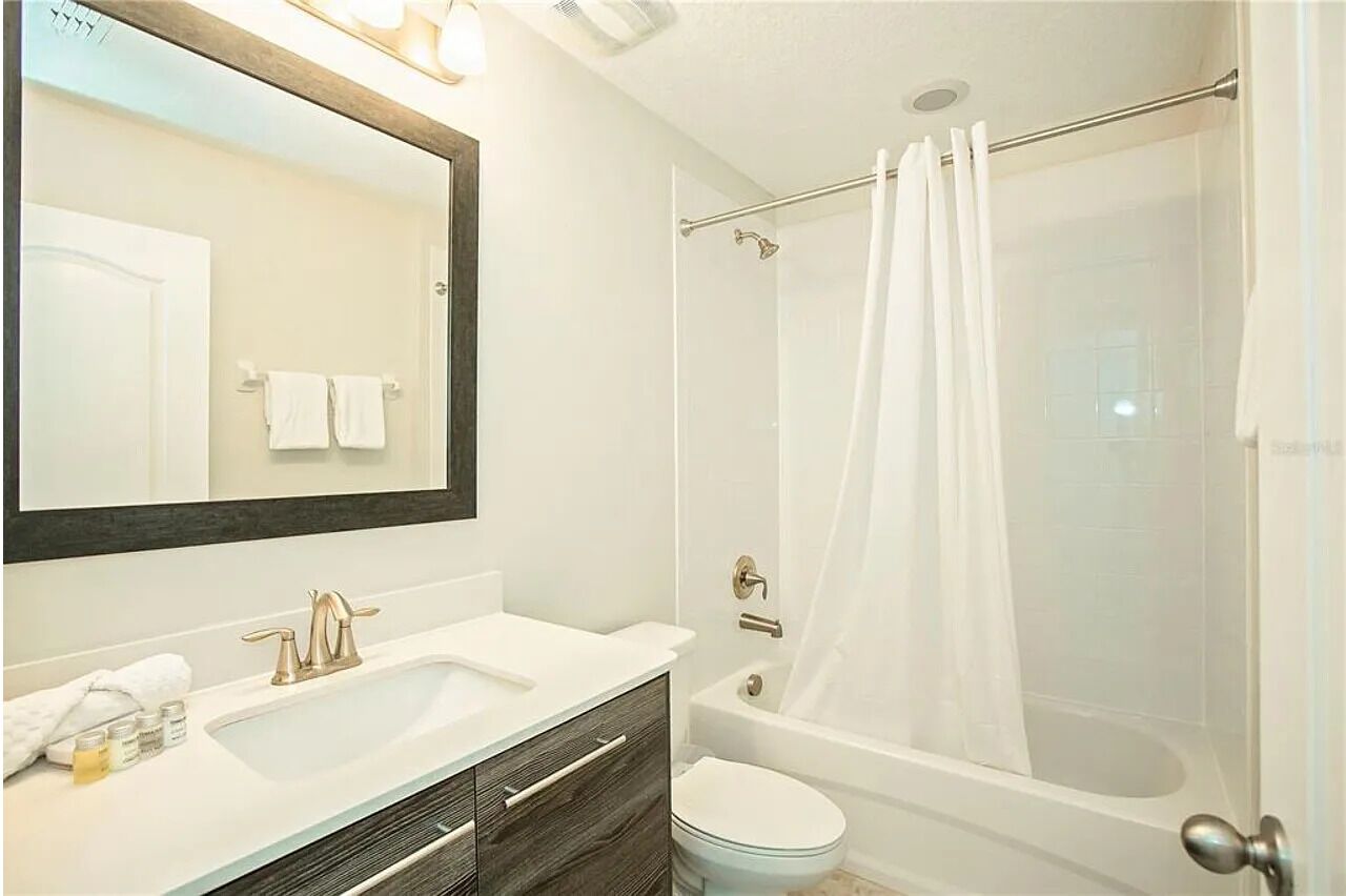 A bathroom with a sink, mirror, vanity, bathtub, and toilet.