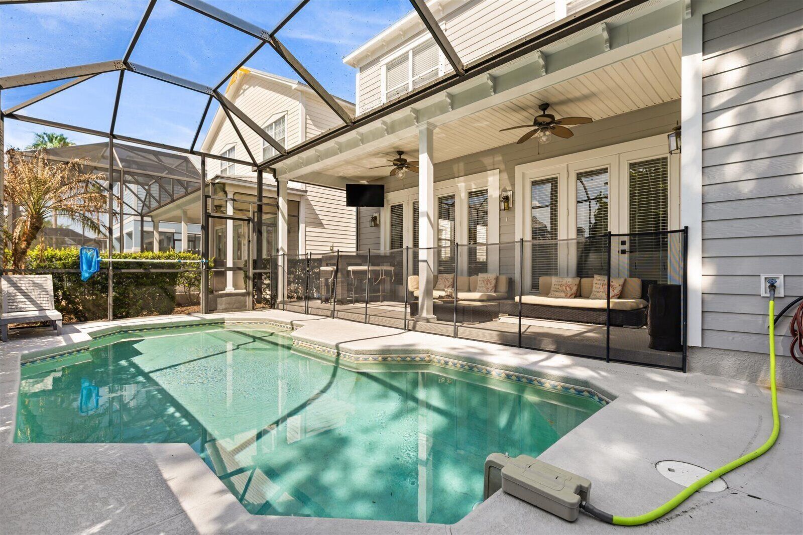 A swimming pool with a glass enclosure, outdoor seating, and a ceiling fan.